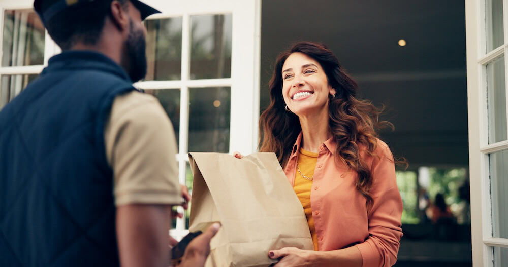 Smiling woman receiving a paper bag delivery at her doorstep