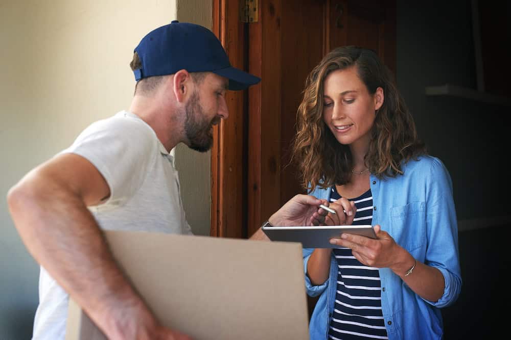 Woman signing on a digital tablet while receiving a package from a delivery worker