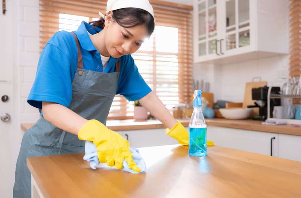 House cleaner wiping a kitchen countertop with cleaning supplies