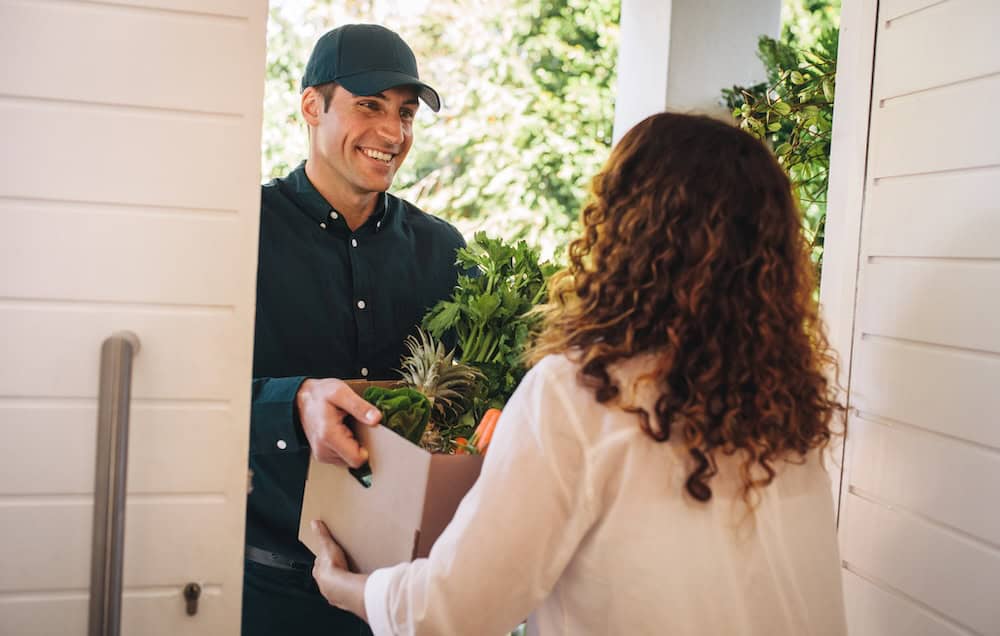 Delivery person handing a package of groceries to a woman at her doorstep