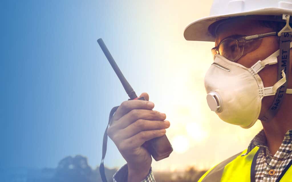 Worker in hard hat and mask talking on a radio.